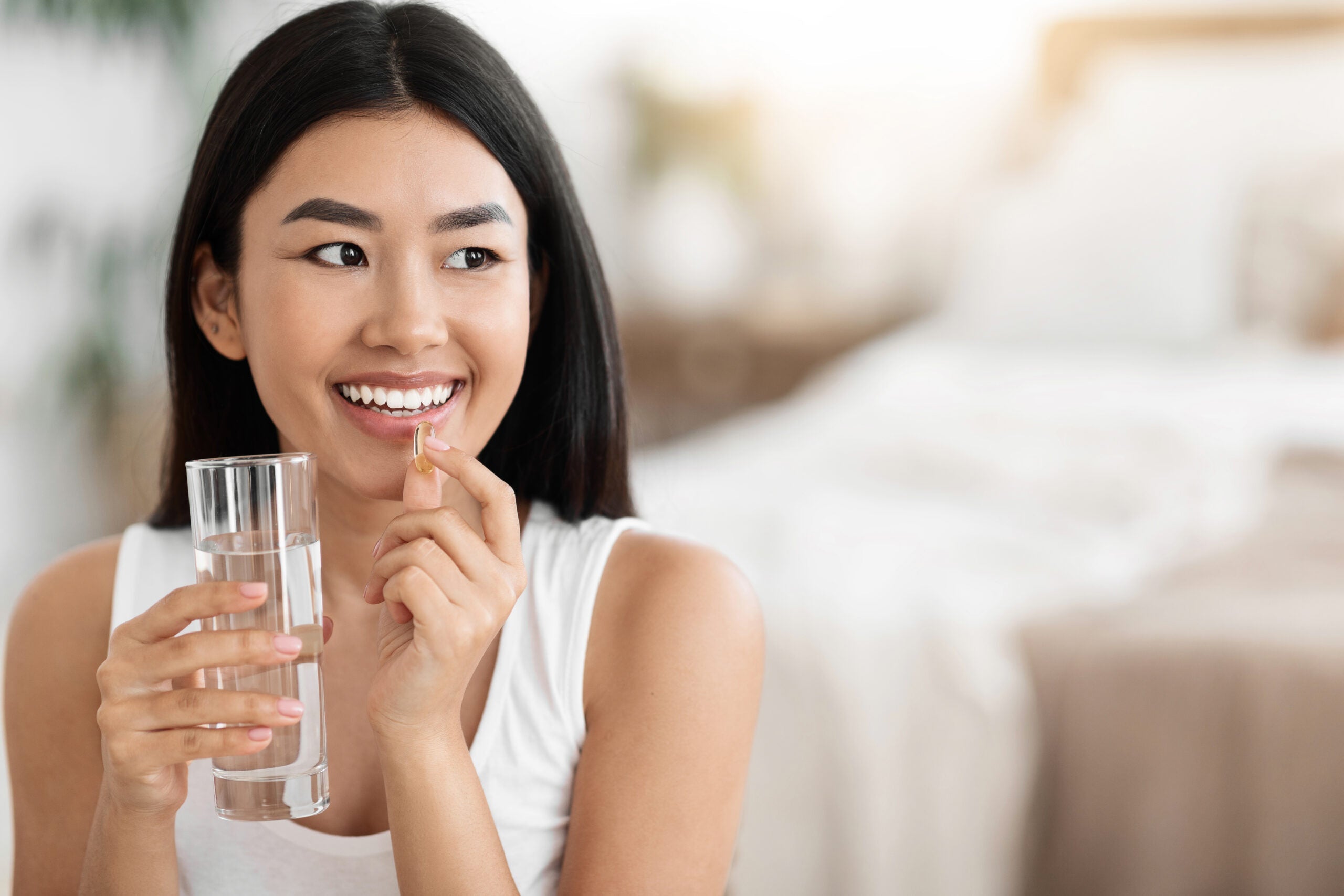 Diet, nutrition, healthy eating concept. Close Up Of Happy Smiling Asian Woman Taking Supplement Pill And Holding Glass Of Fresh Water In Morning, copy space