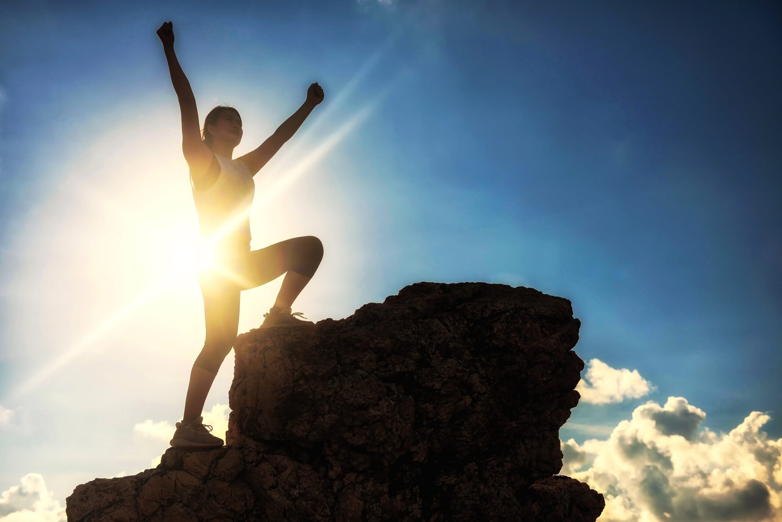 Silhouette sport hiking woman raise victory hands and stand on top of hill during sunset after climbing to mountain summit peak with copy space for text. Success to goal. Business and Health concept.