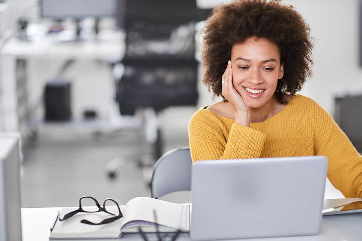 A woman smiles while cradling her face and reading a computer screen