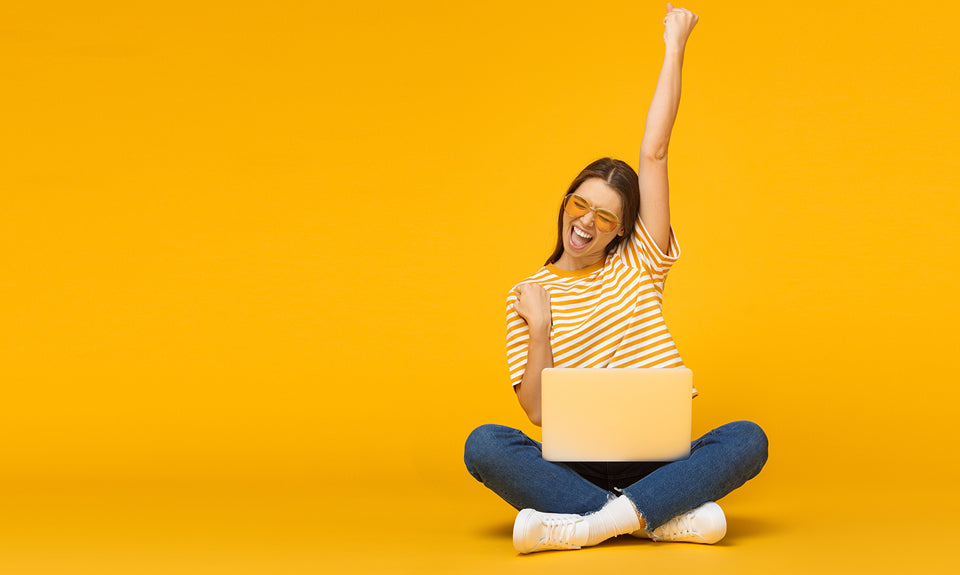 A woman wearing yellow sitting crosslegged in front of a yellow wall with a portable computer in her lap