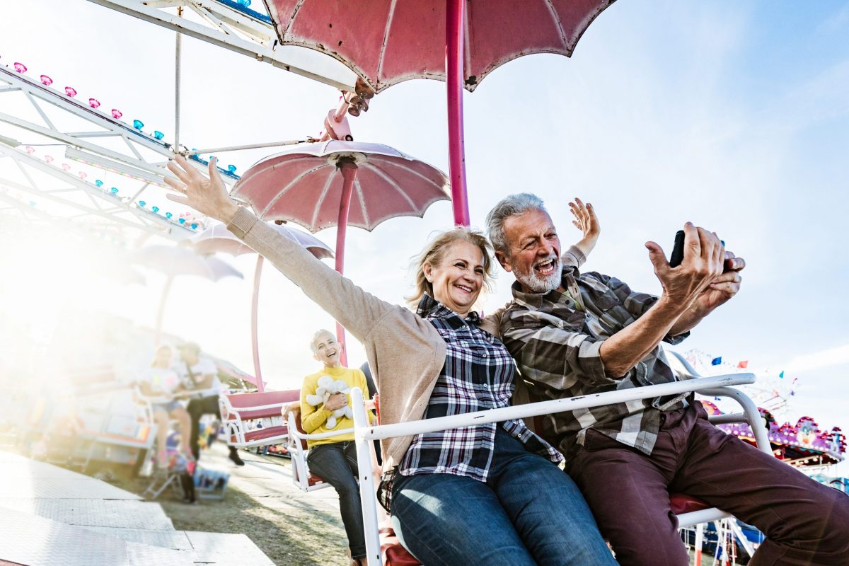 Happy mature couple having fun while taking a selfie with cell phone during amusement park ride.