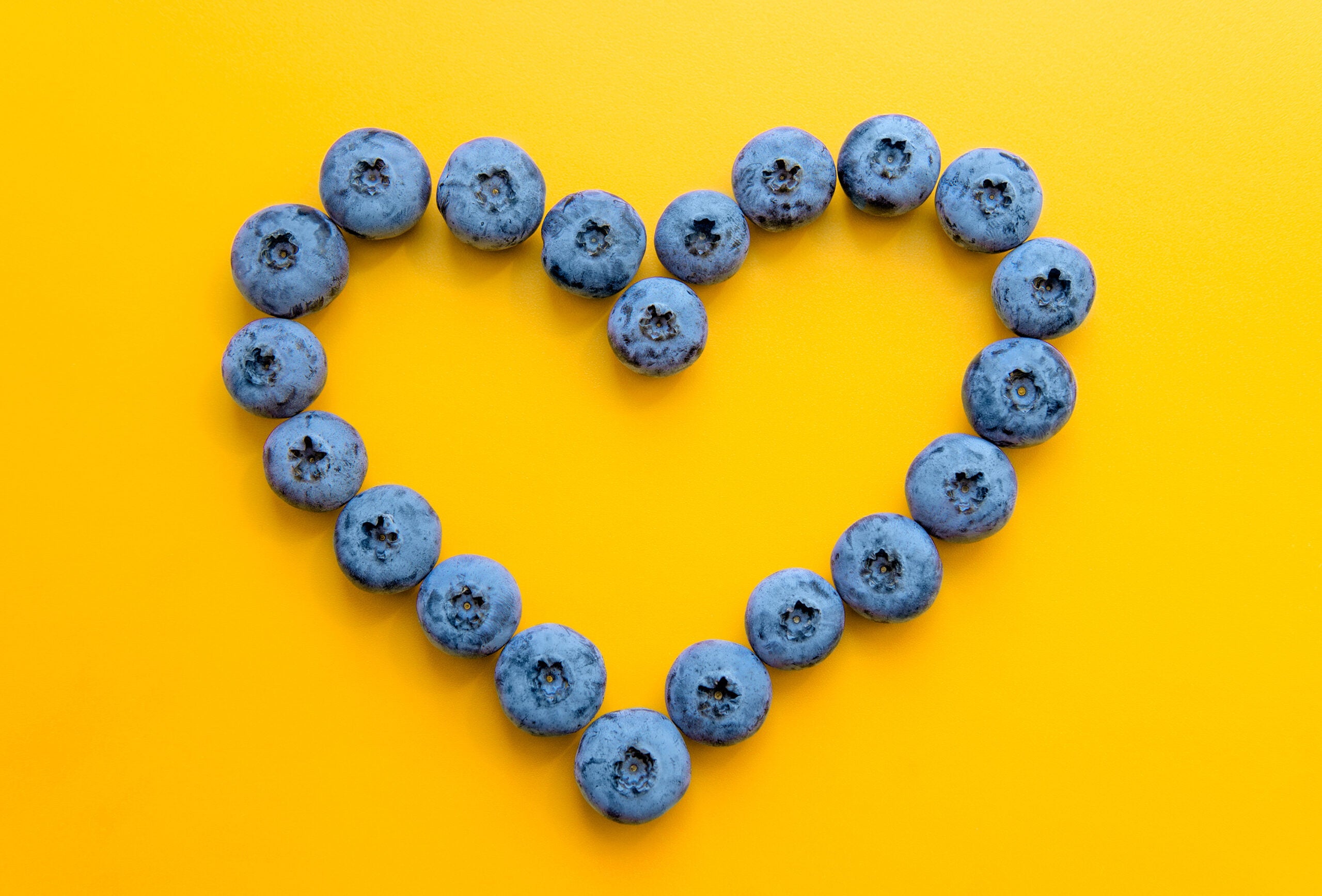 Heart symbol made from blueberries on a yellow background. Heart health concept.
