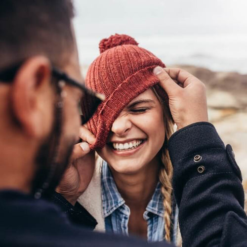 A man adjusts the beanie hat on his girlfriend on a beach