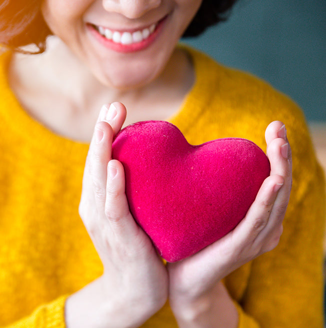 A woman in a yellow sweatshirt cradles a red felted heart