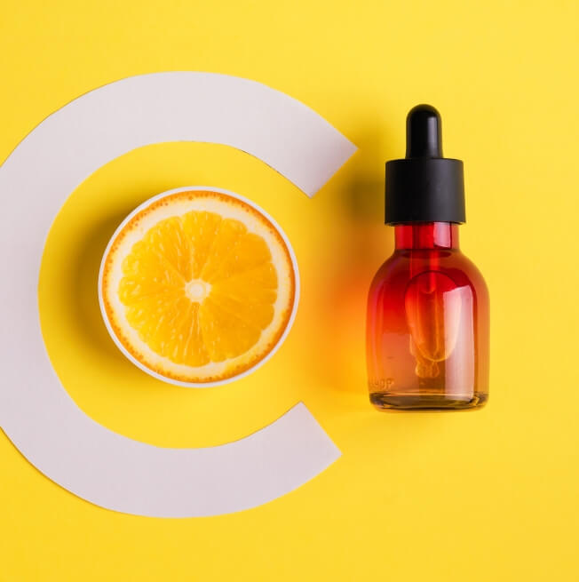 A slice of lemon and a bottle with dropper arranged on a yellow background