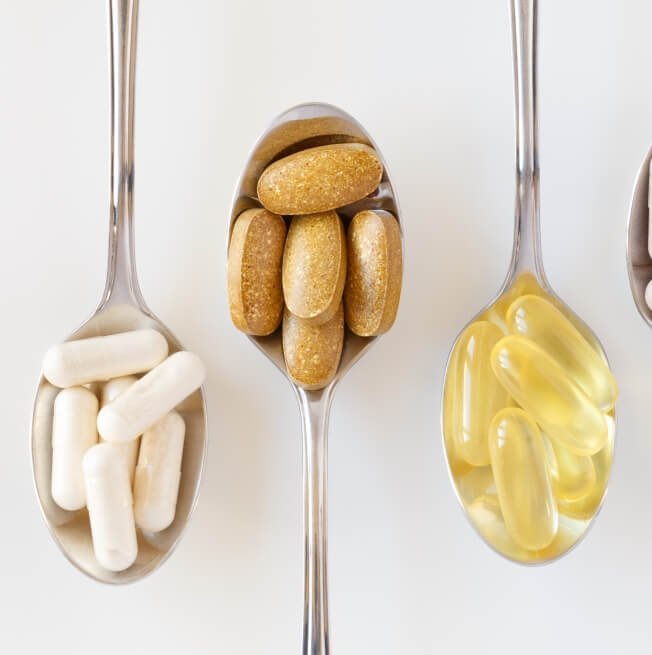 A closeup image of three spoons, each filled with pills of different colors