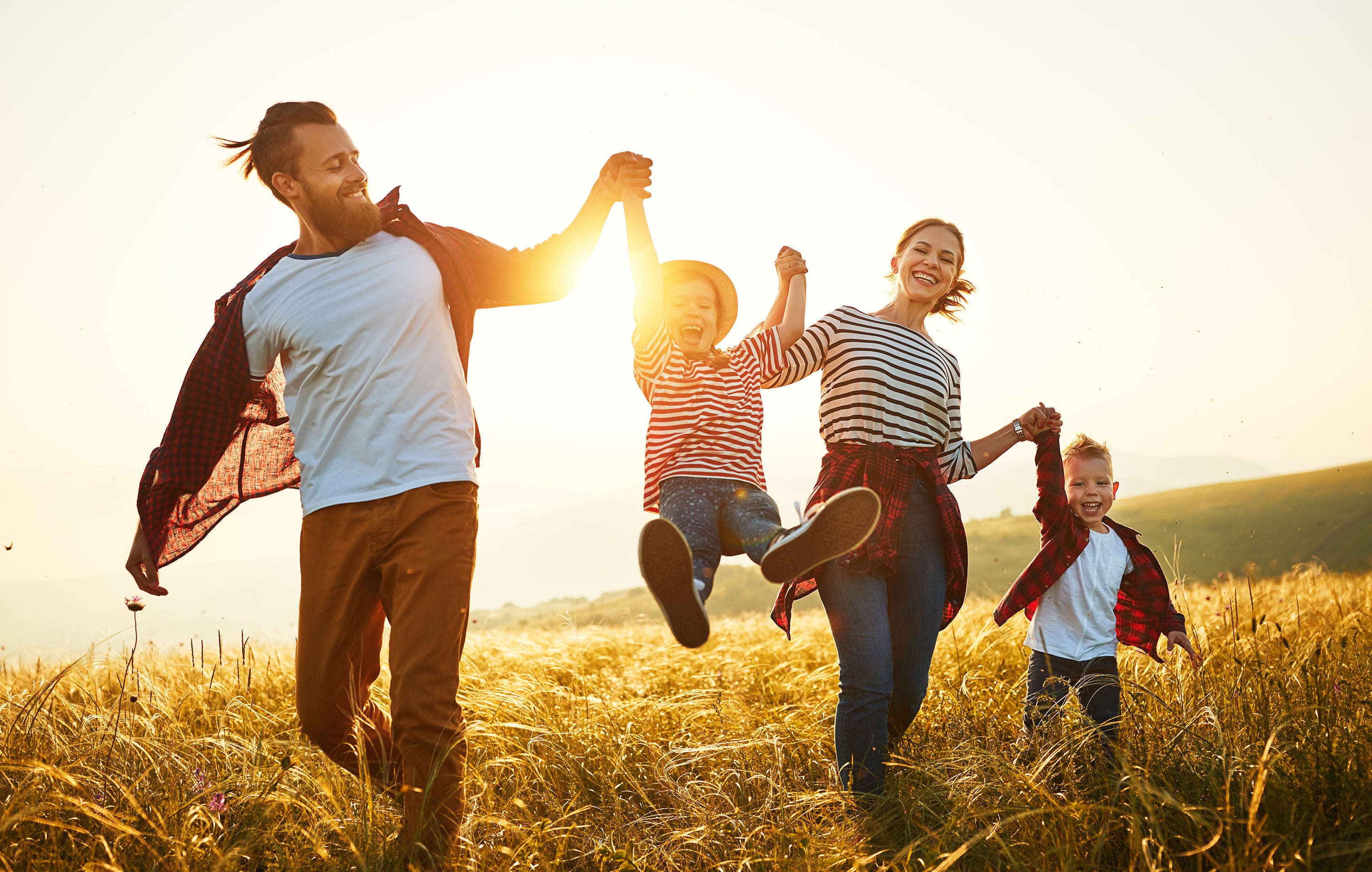 A joyful family plays together in a field of grass during sunset